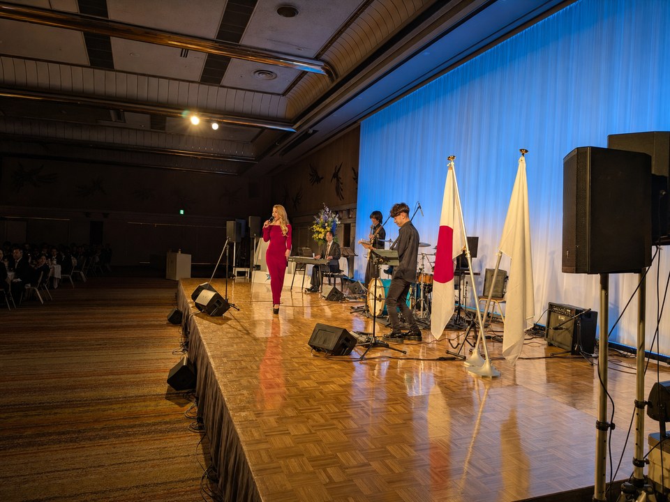 青い舞台照明の表彰式会場で赤いドレスの女性歌手とバンドが演奏するステージ